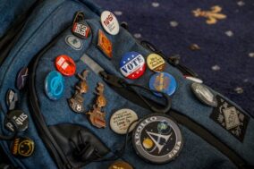 Detailed close-up of a blue backpack adorned with various creative pins and badges.