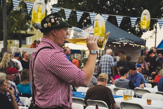 Man enjoying a large beer mug at an Oktoberfest celebration outdoors with a lively crowd.