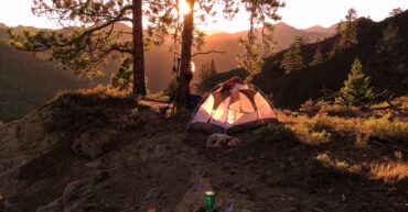 Tent nestled in forested mountains at sunrise, capturing the serene beauty of camping outdoors.