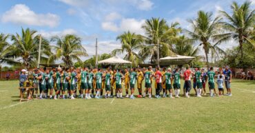 Two youth soccer teams exchange handshakes on a sunny day under palm trees.